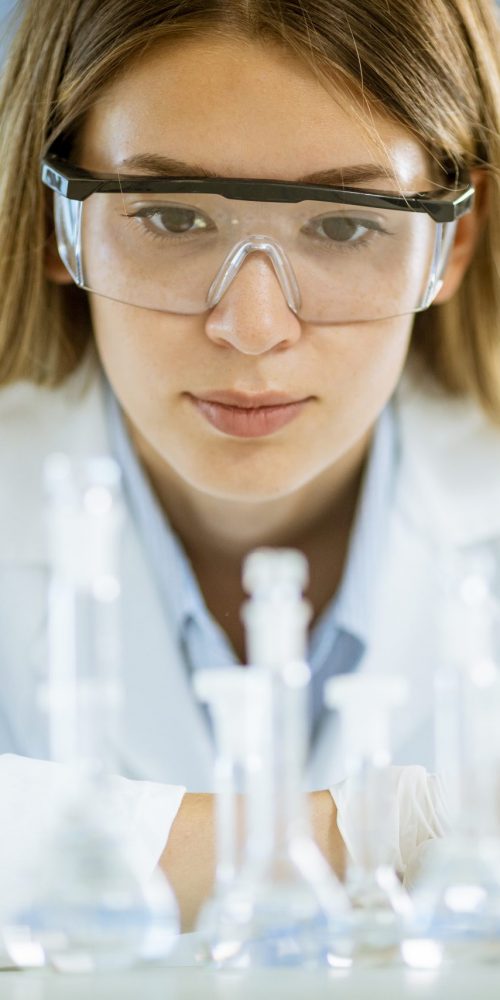 Young female medical or scientific researcher looking at a flasks with solutions in a laboratory